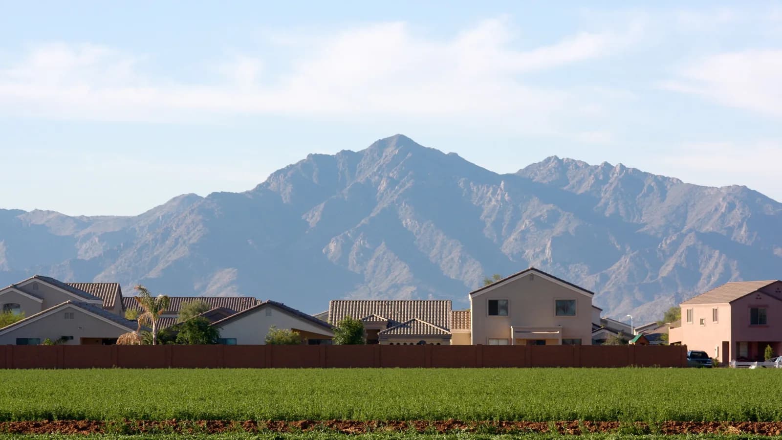 New tile-roofed homes in Avondale behind a green field, with the Sierra Estrella mountains rising behind